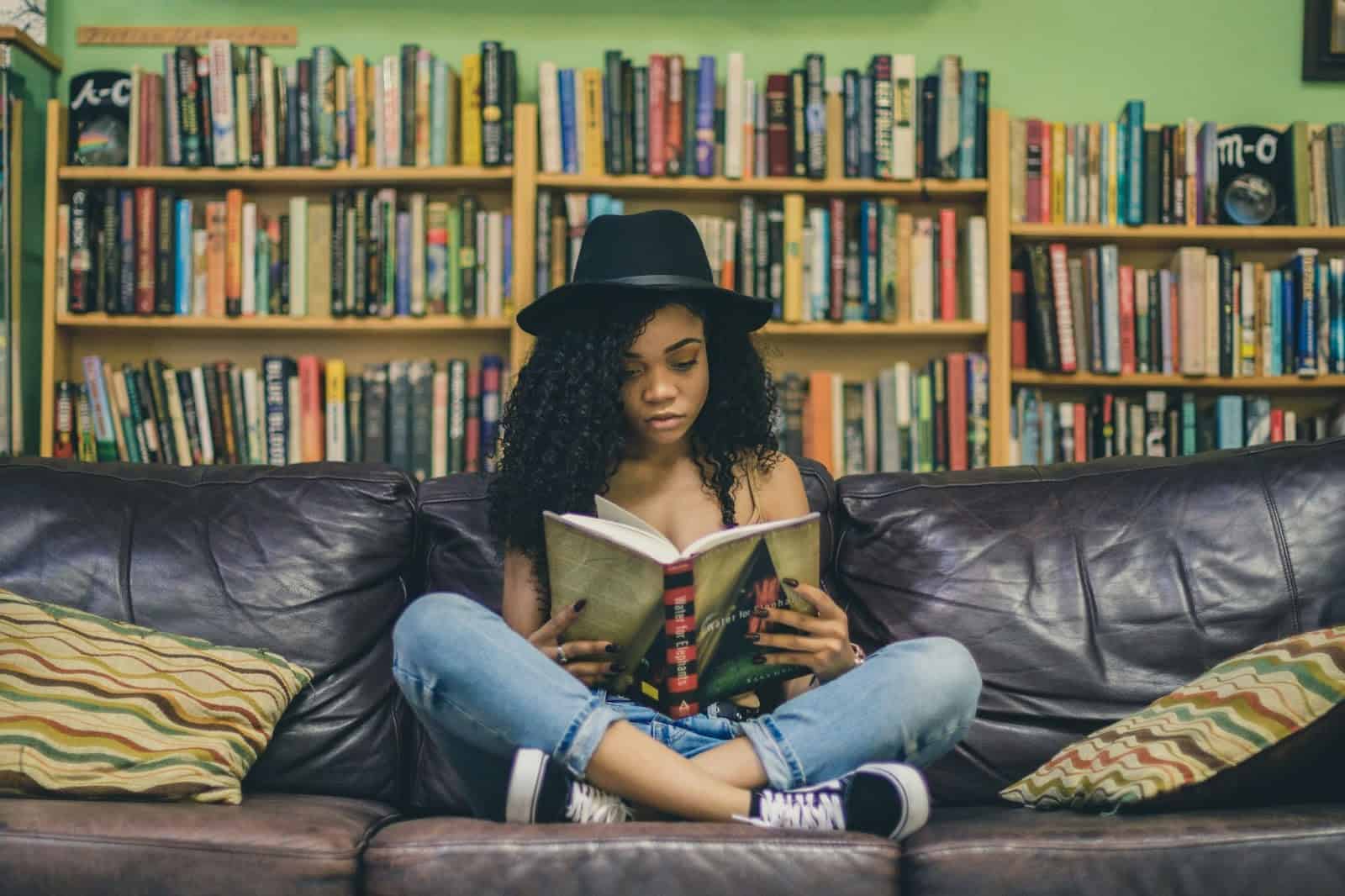 Person reading a book on a couch in front of bookshelves