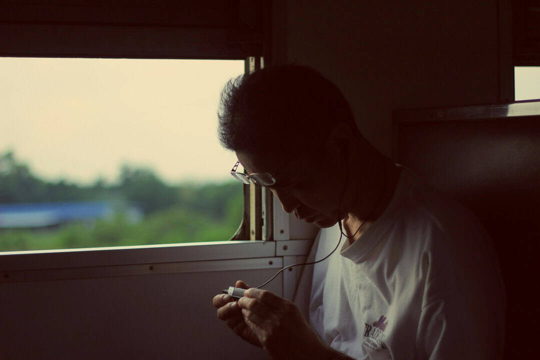 Person with headphones looking at a device by a train window